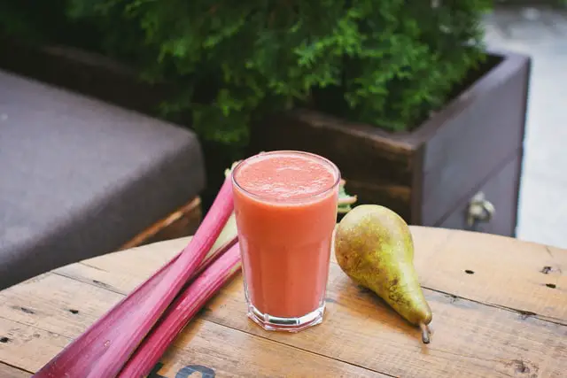 a wooden table with pear and rhubarb, and a glass filled with smoothie